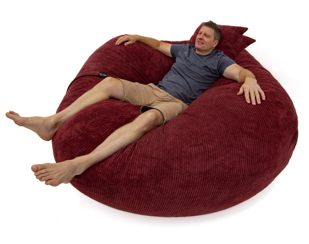 Man relaxing on a large red bean bag chair against a white background