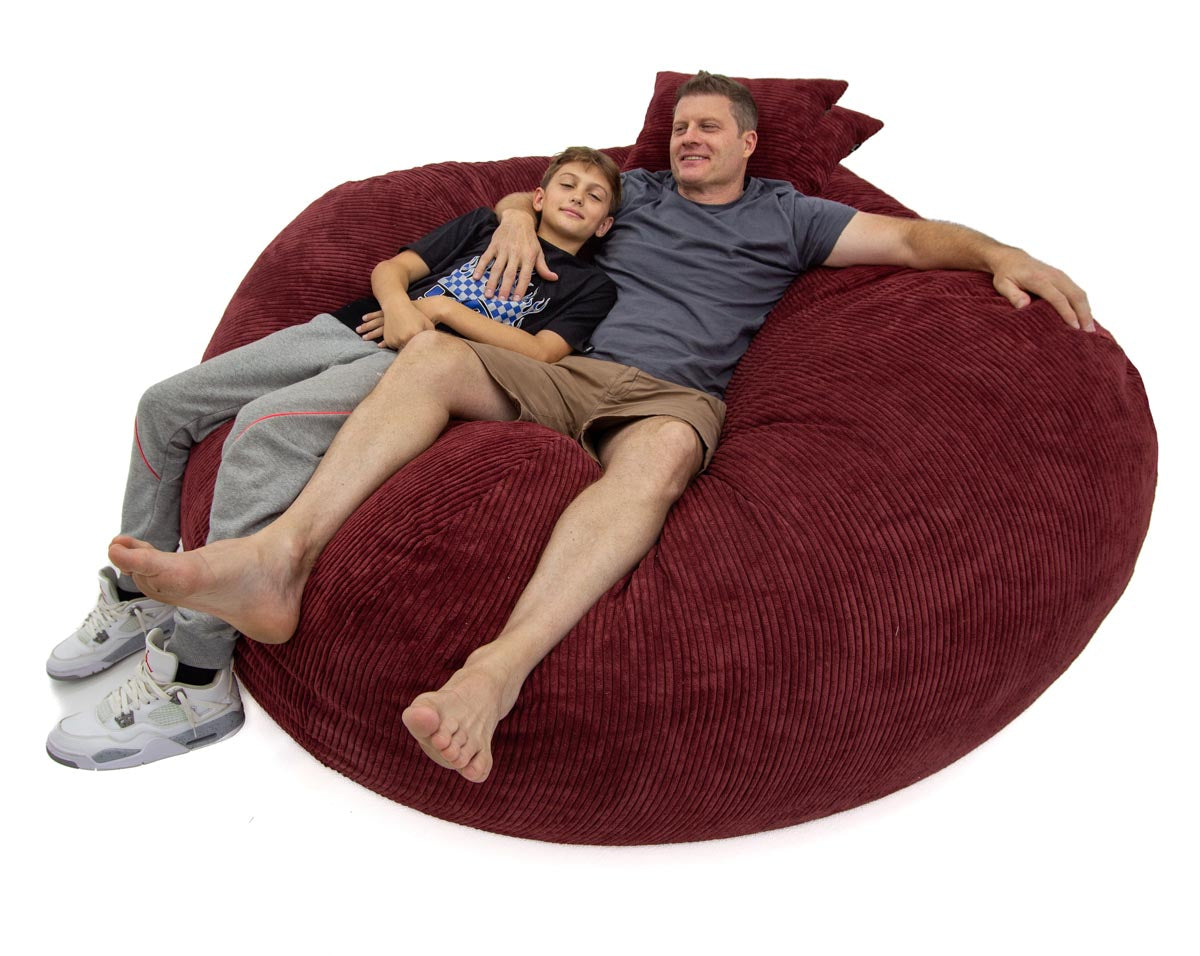 Two people lying on a large red bean bag chair against a white background