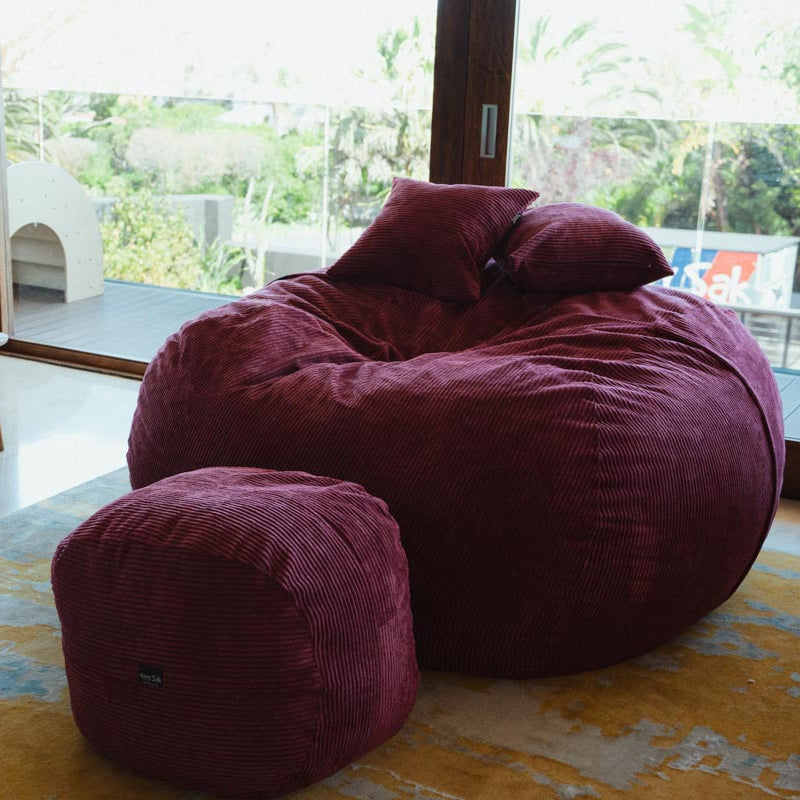 Maroon bean bag chair with ottoman on a rug in a room with large windows.
