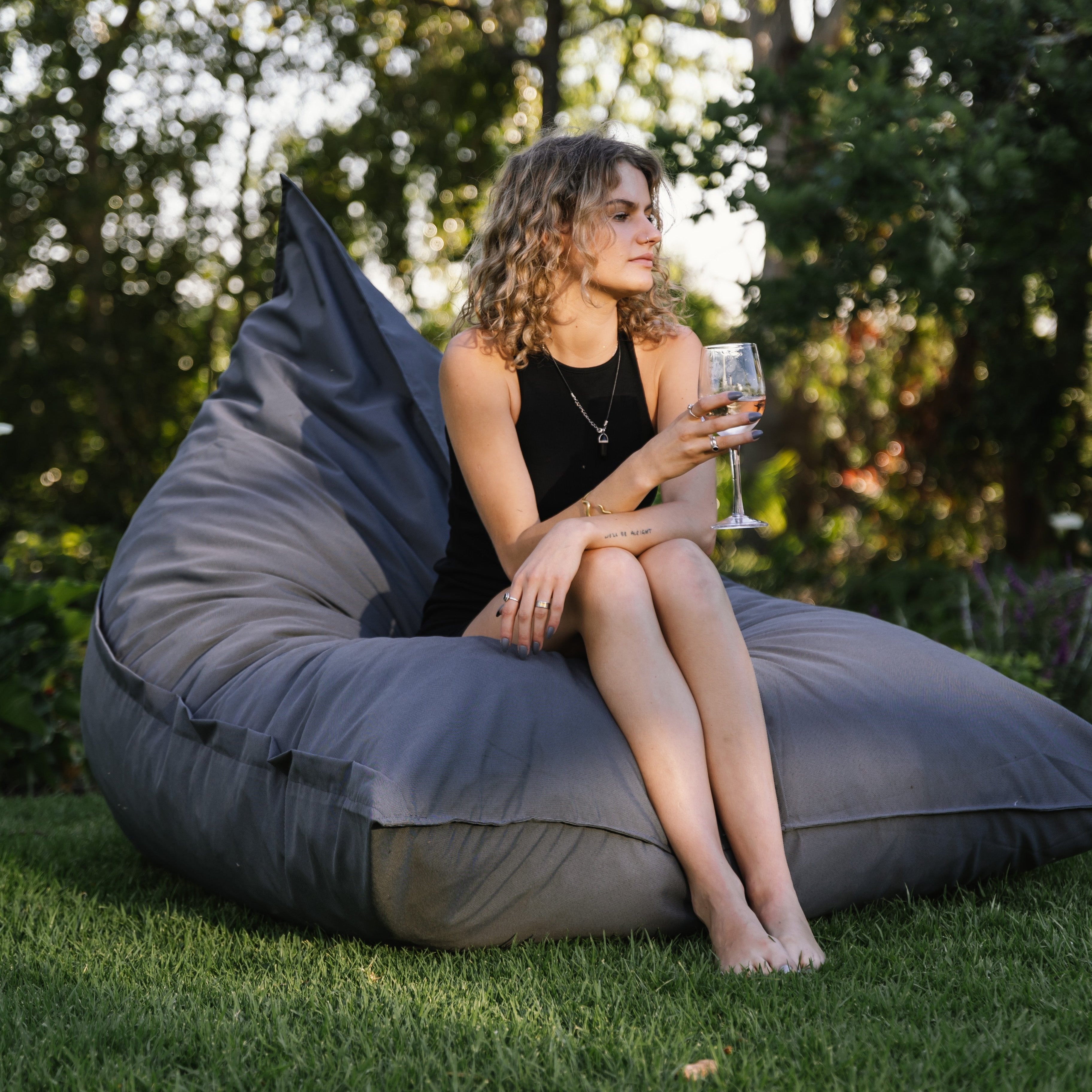 A person sitting on a gray Flip Sak outdoor bean bag chair holding a glass of wine.