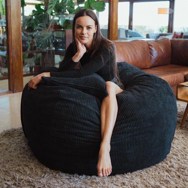 Woman sitting on a black bean bag chair in a modern living room.
