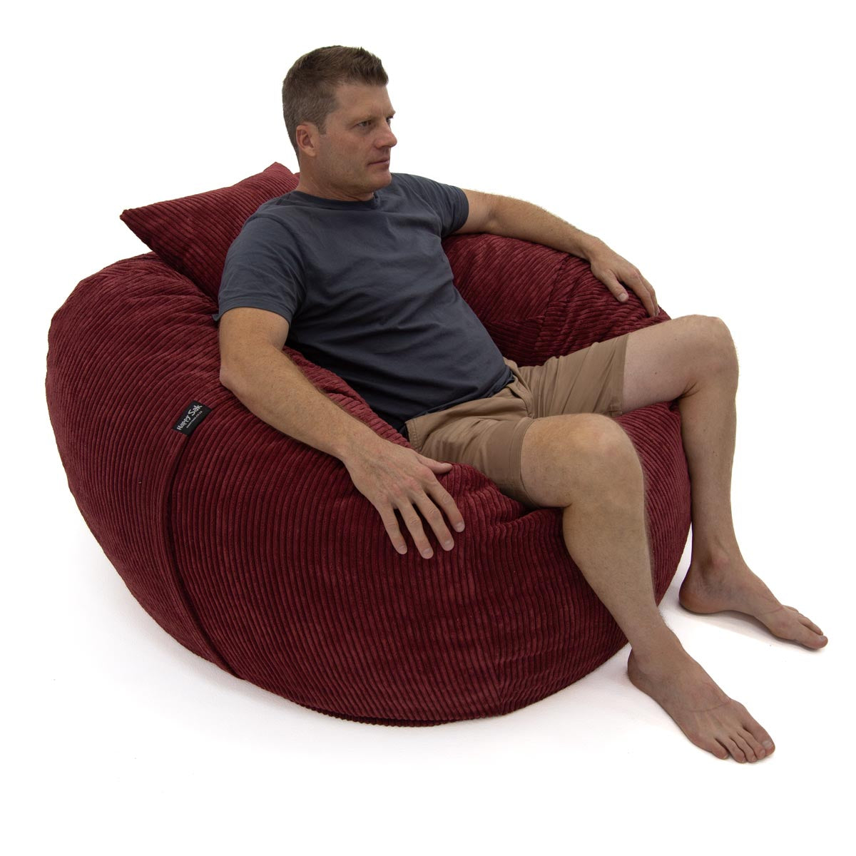Man sitting on a large red bean bag chair against a white background