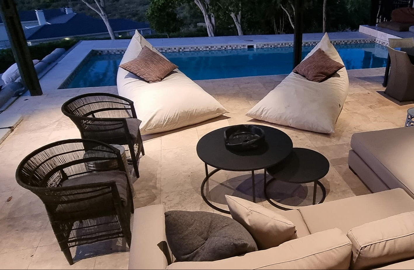 Outdoor patio area with beige sectional sofa, black chairs, and a round table by a pool.