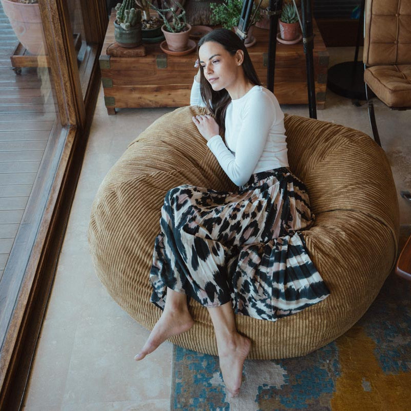 Woman sitting on a bean bag chair in a cozy room with plants and furniture.