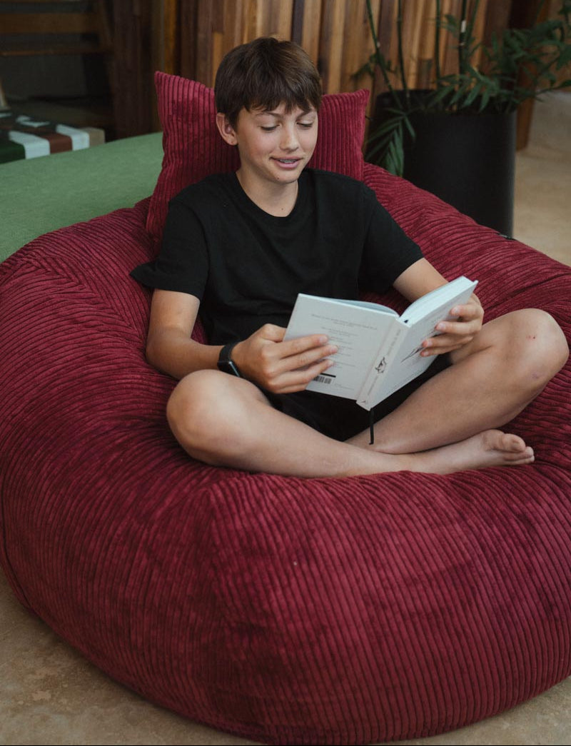 Child reading a book on a red bean bag chair in a cozy room.