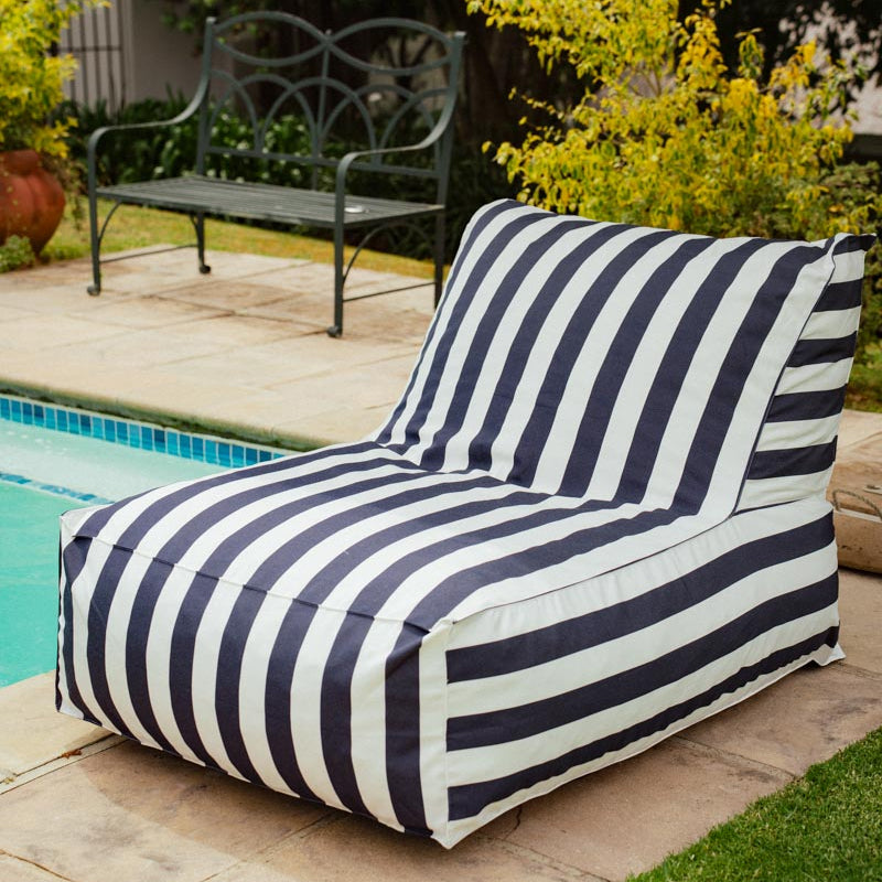 Navy and white striped bean bag chair by a poolside with greenery in the background