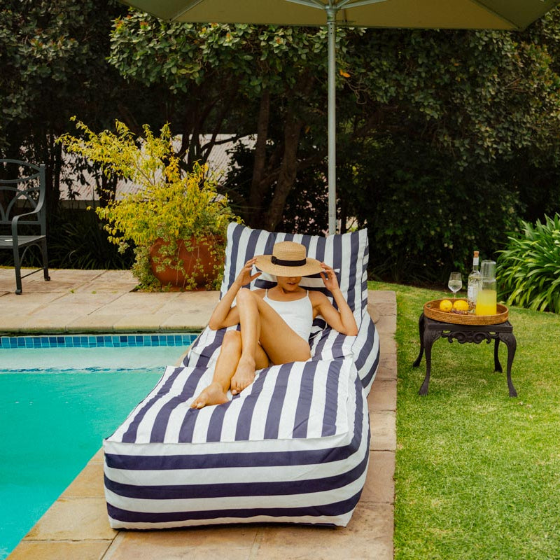Woman relaxing on a striped lounge chair by a poolside with a scenic background