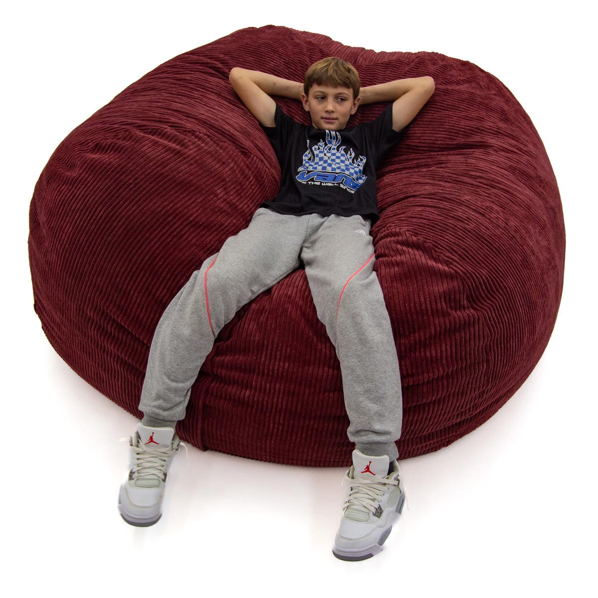Child sitting on a large red bean bag chair against a white background