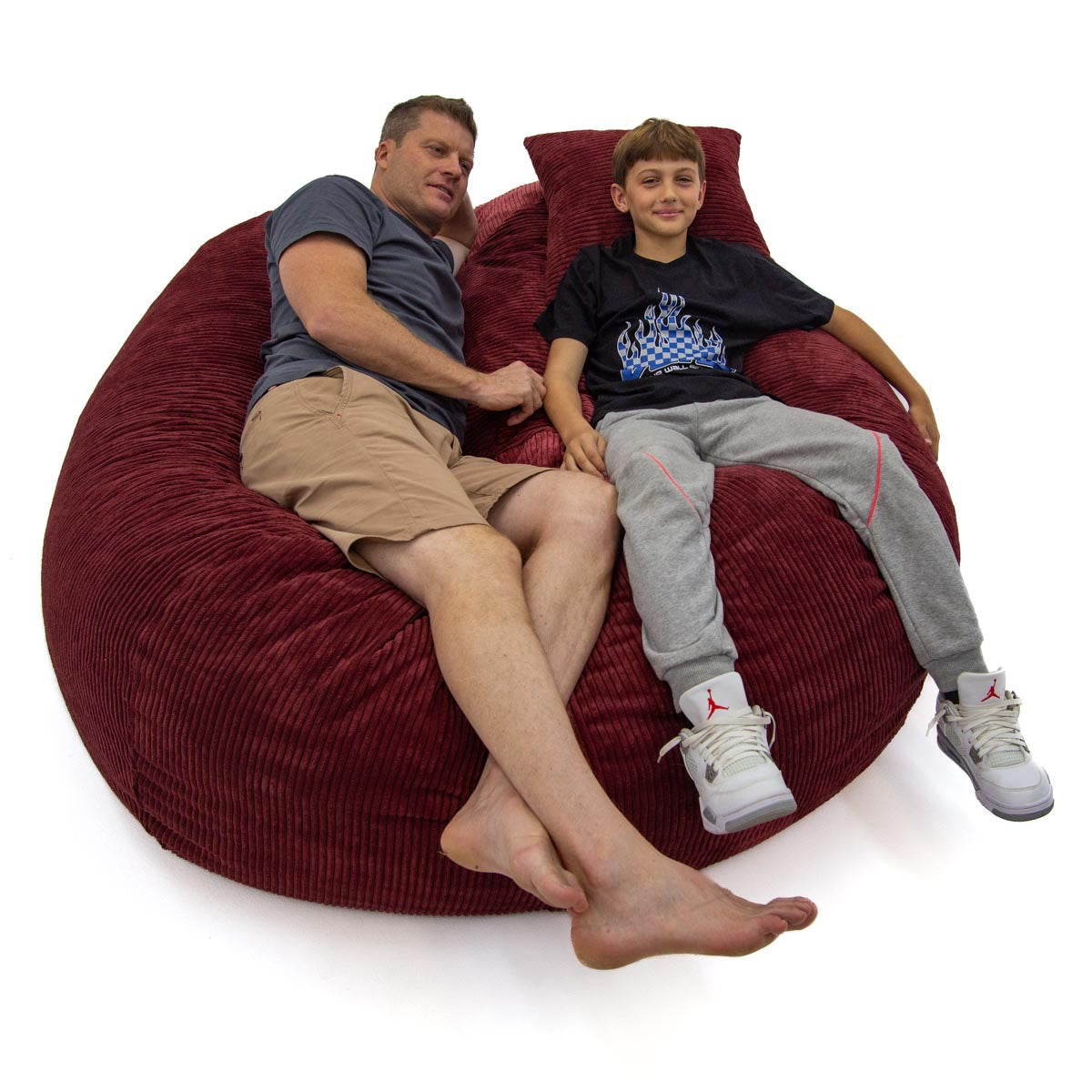 Man and child sitting on a large red bean bag chair against a white background