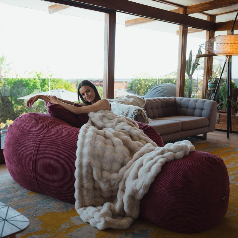 Woman sitting on a large bean bag chair in a modern living room with large windows.