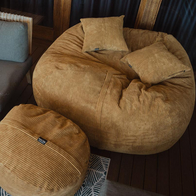 Brown bean bag chair with cushions on a wooden floor.