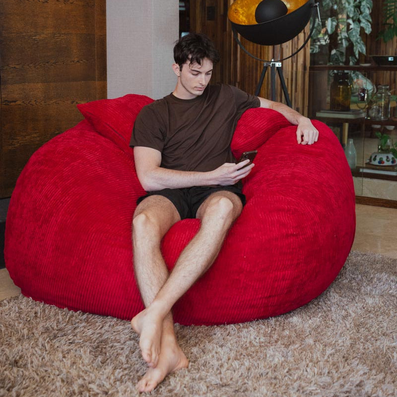 Man sitting on a red bean bag chair in a room with wooden walls and decor.