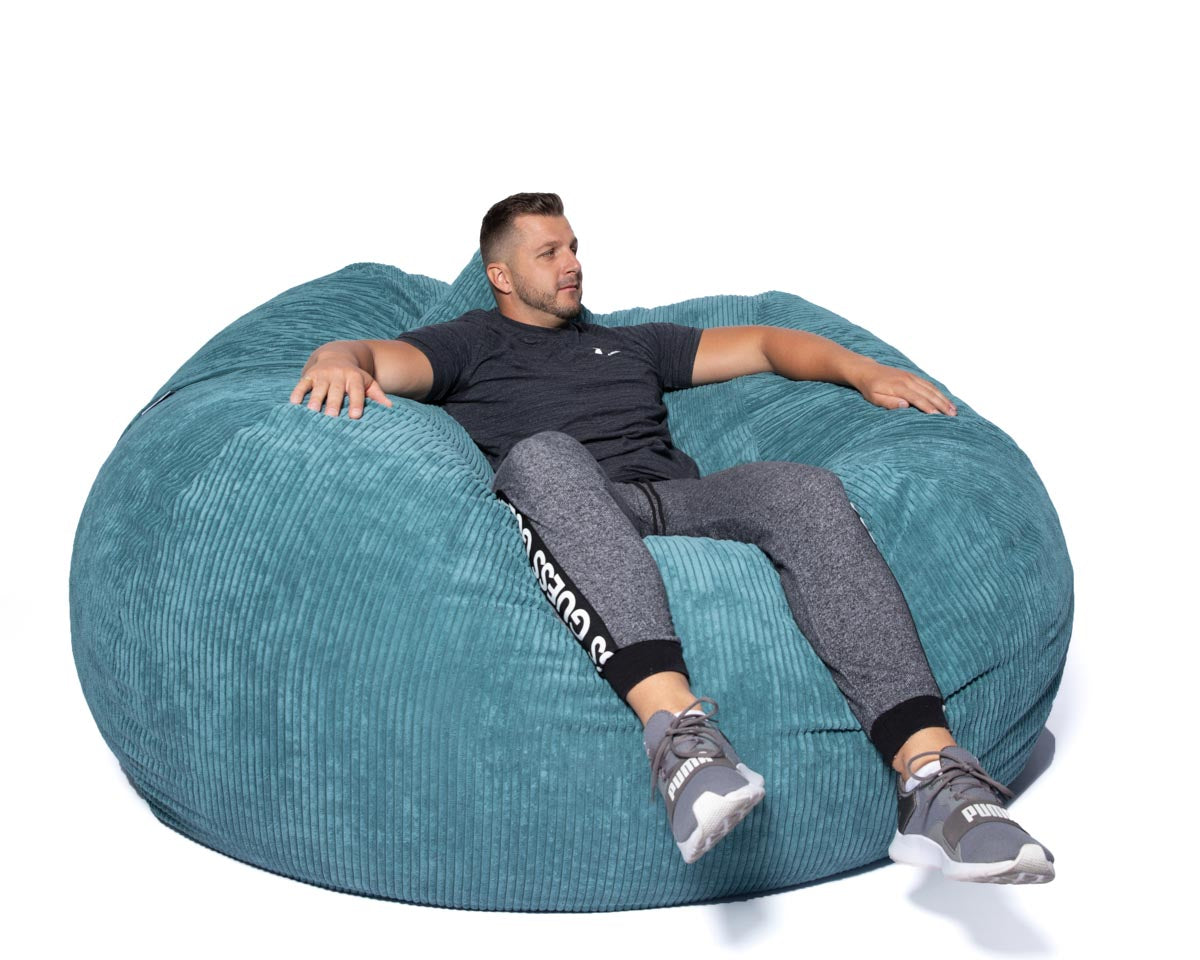 Man sitting on a large teal bean bag chair against a white background