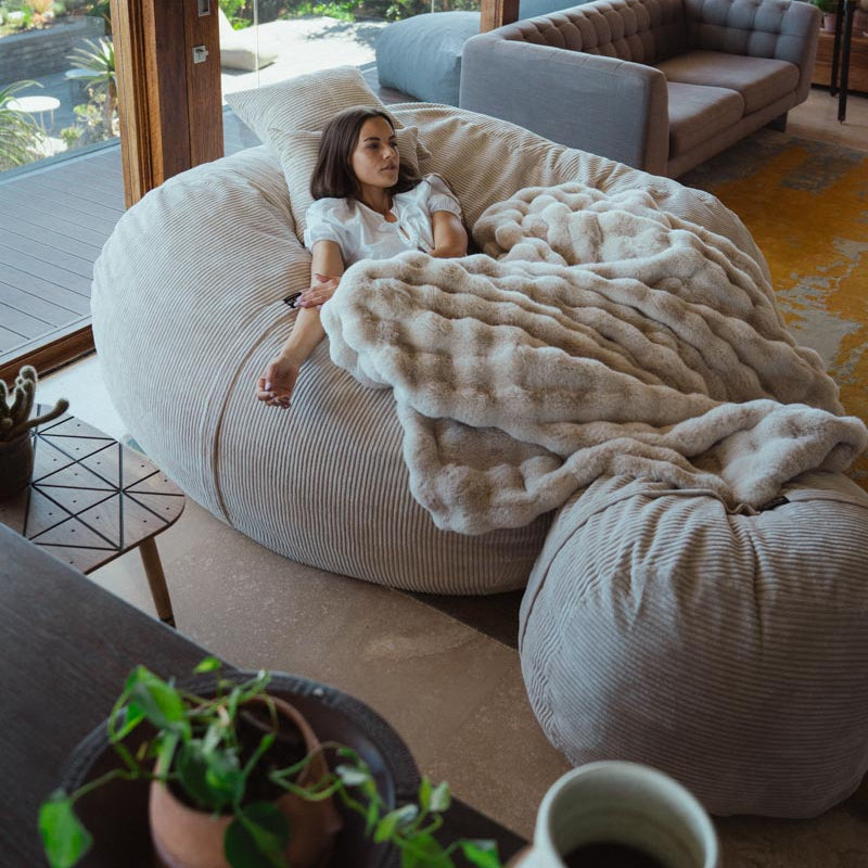 Woman sitting on a large bean bag chair in a modern living room with large windows.