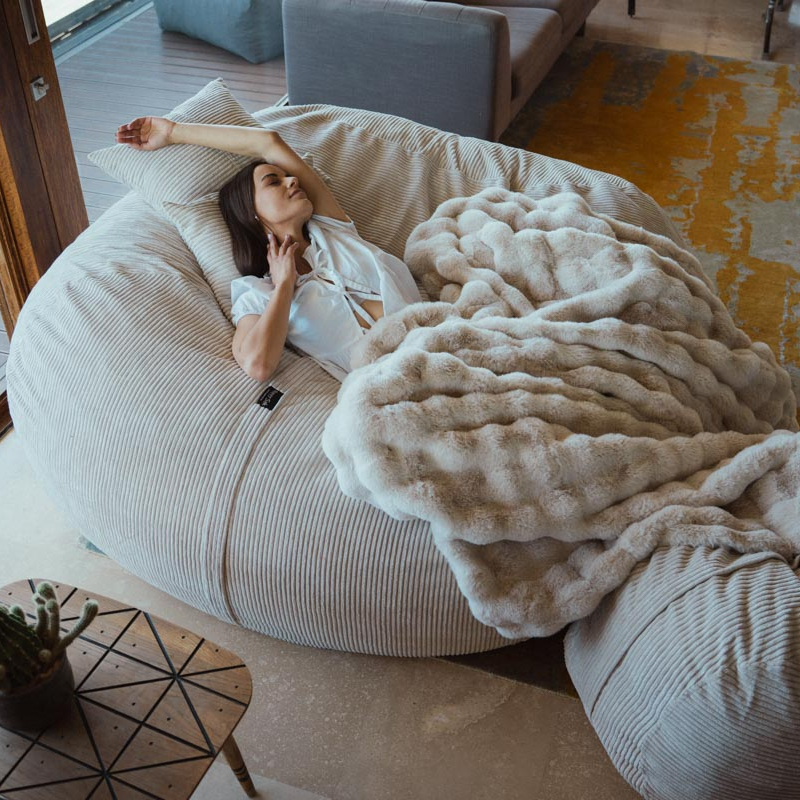 Woman lying on a bean bag chair with a blanket in a cozy living room.
