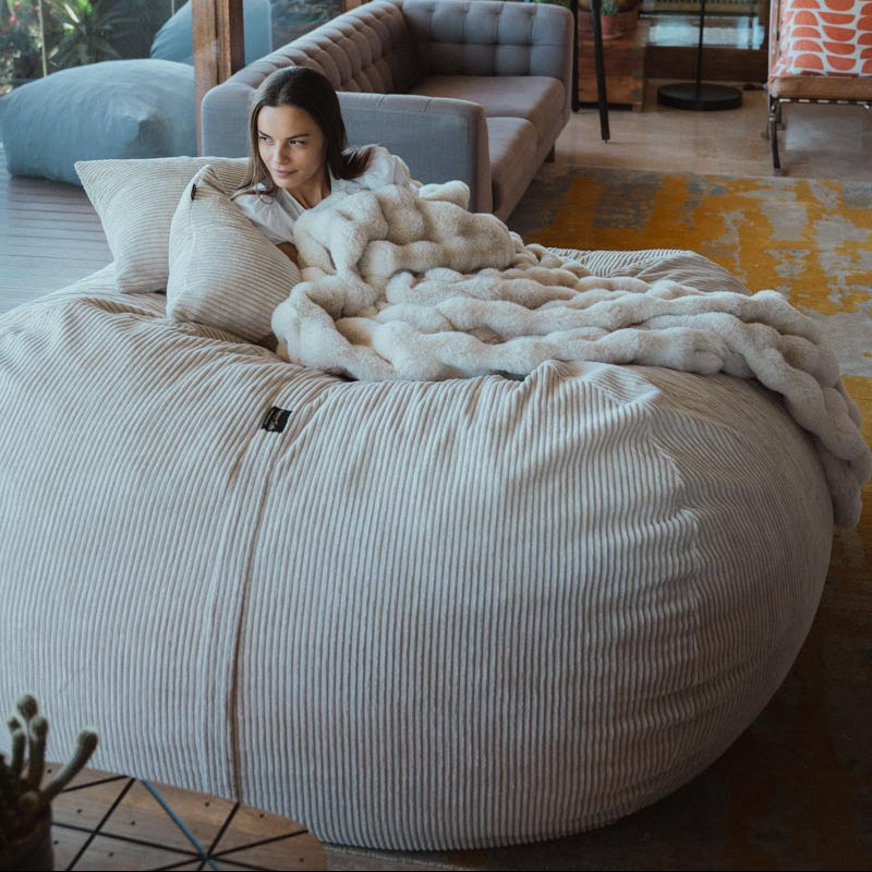Woman lying on a large bean bag chair in a modern living room with large windows.