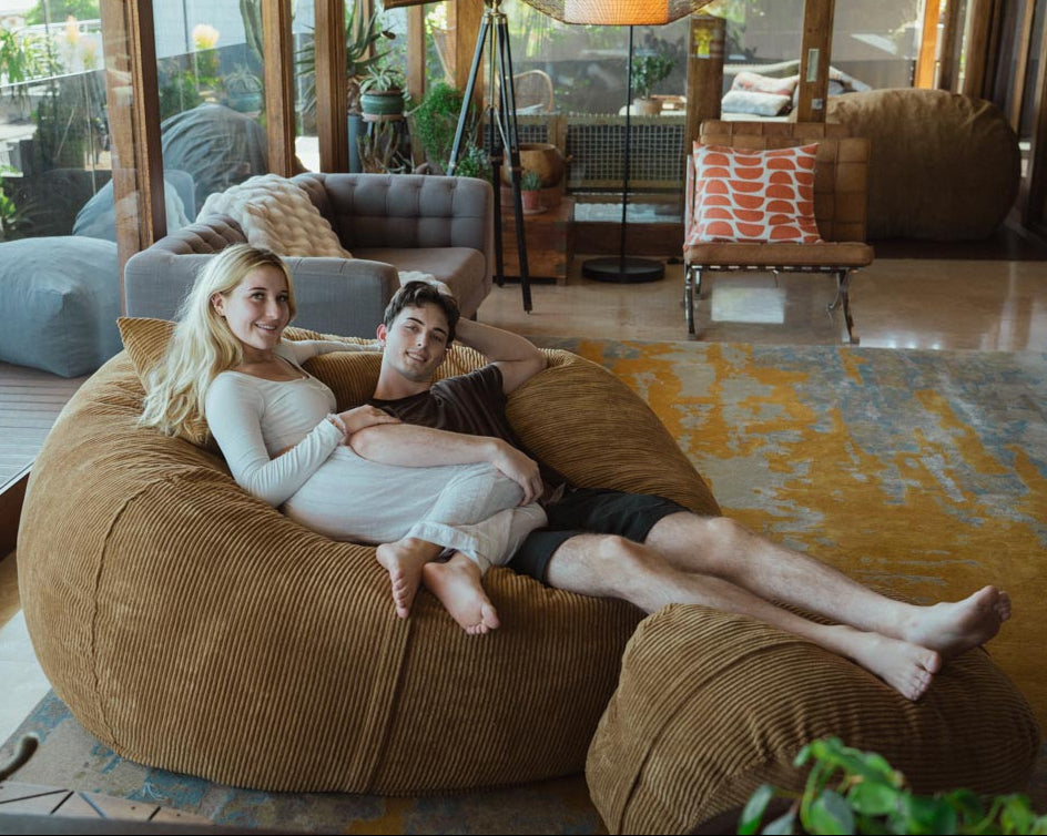 Two people sitting on a large brown bean bag in a modern living room.