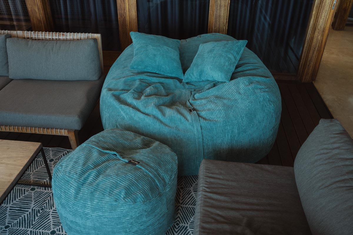 Turquoise bean bags and ottoman in a room with wooden flooring and dark curtains.