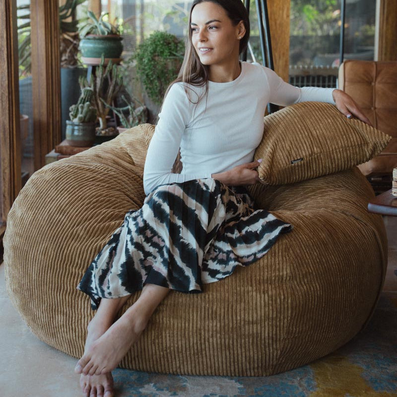 Woman sitting on a large brown bean bag chair in a cozy indoor setting.