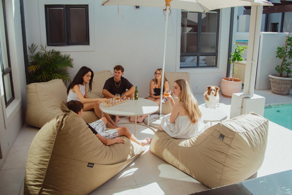 Group of people sitting around a table outdoors with bean bags and an umbrella.