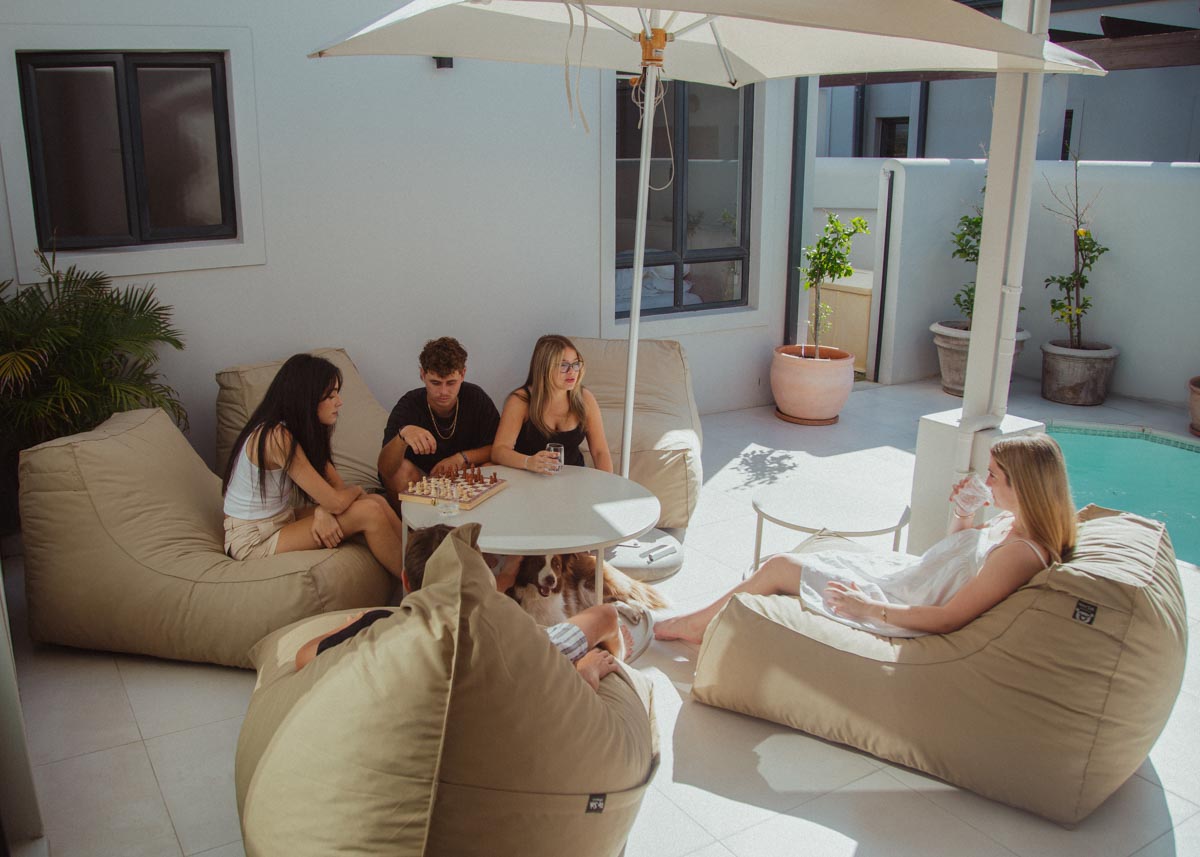 People sitting on bean bags by a poolside with an umbrella