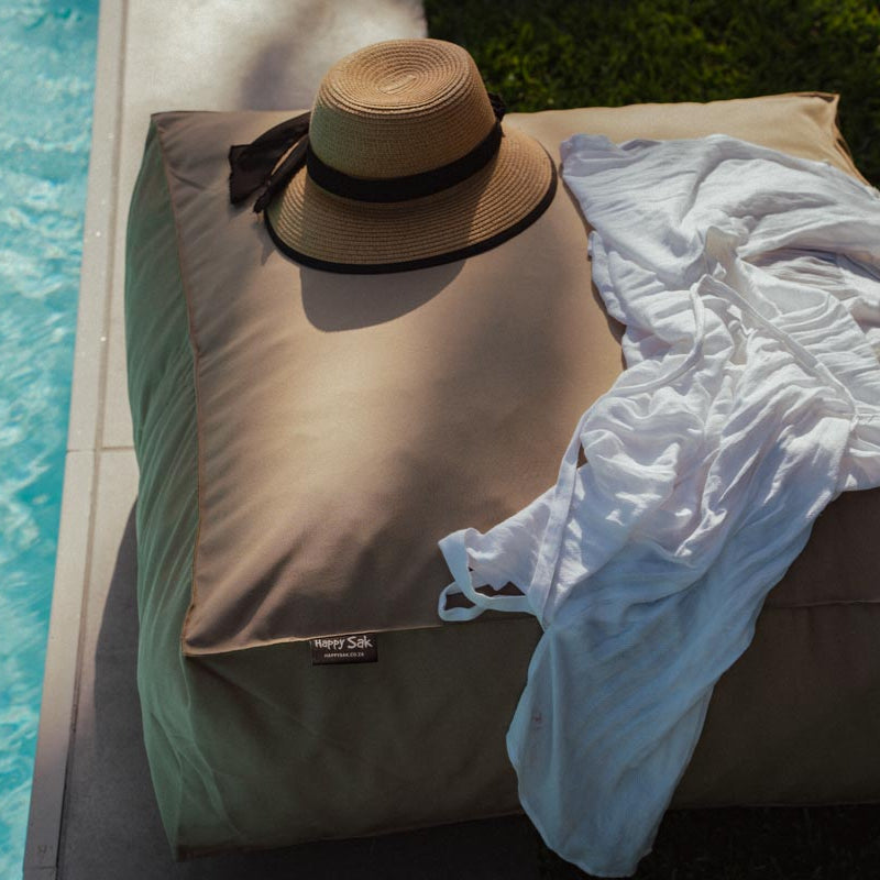 Beige lounge chair with a straw hat and white towel by a poolside