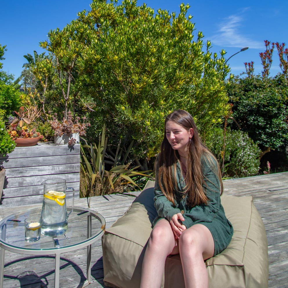 Woman sitting on a patio chair with a glass of lemon water, surrounded by greenery.