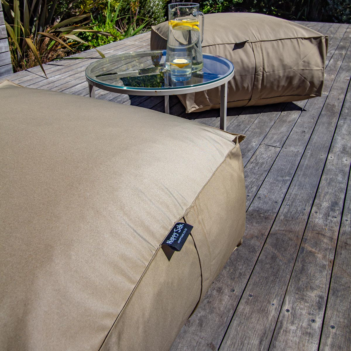 Beige outdoor bean bag chair on a wooden deck with a small table and pillows in the background.