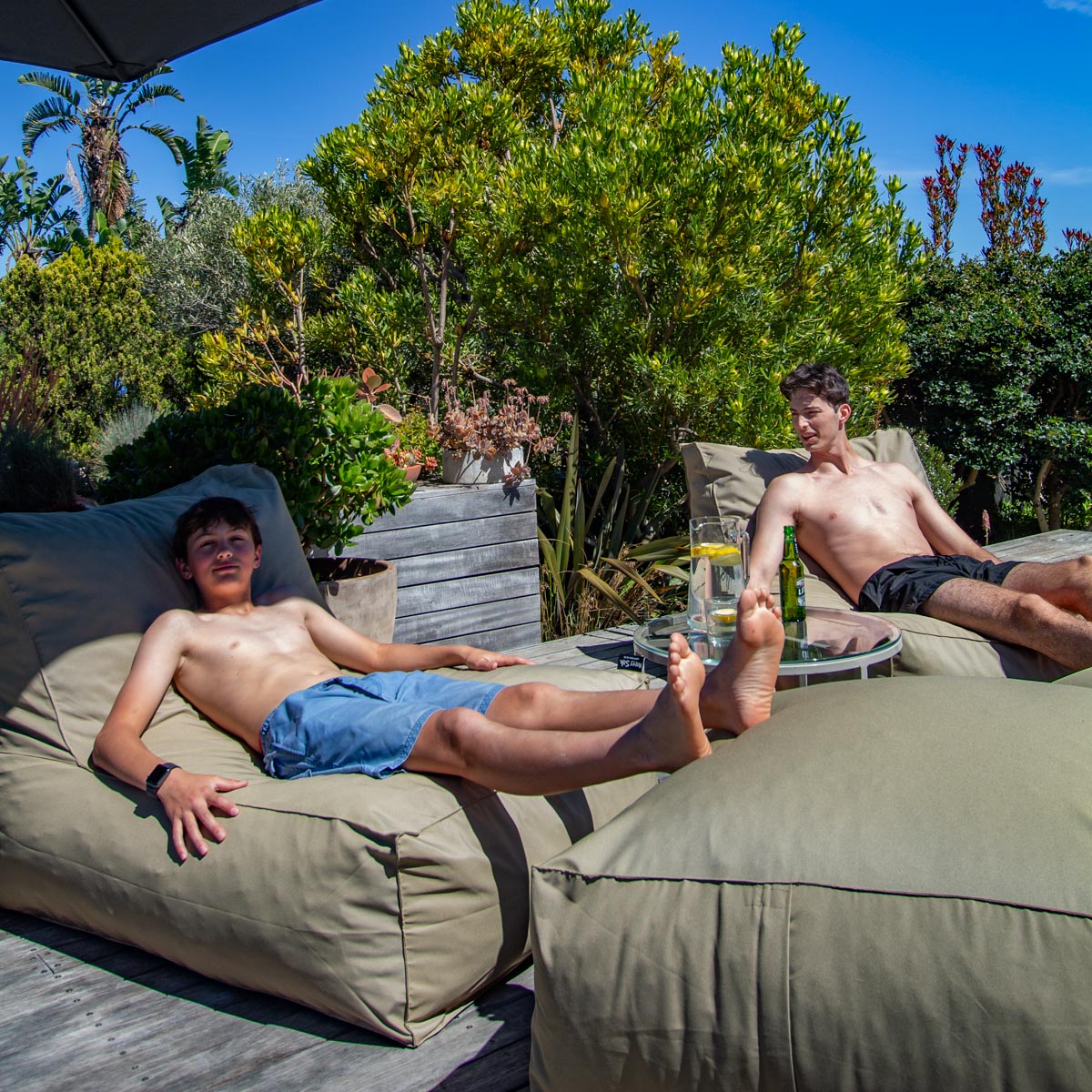 Two men relaxing on bean bags outdoors with drinks.