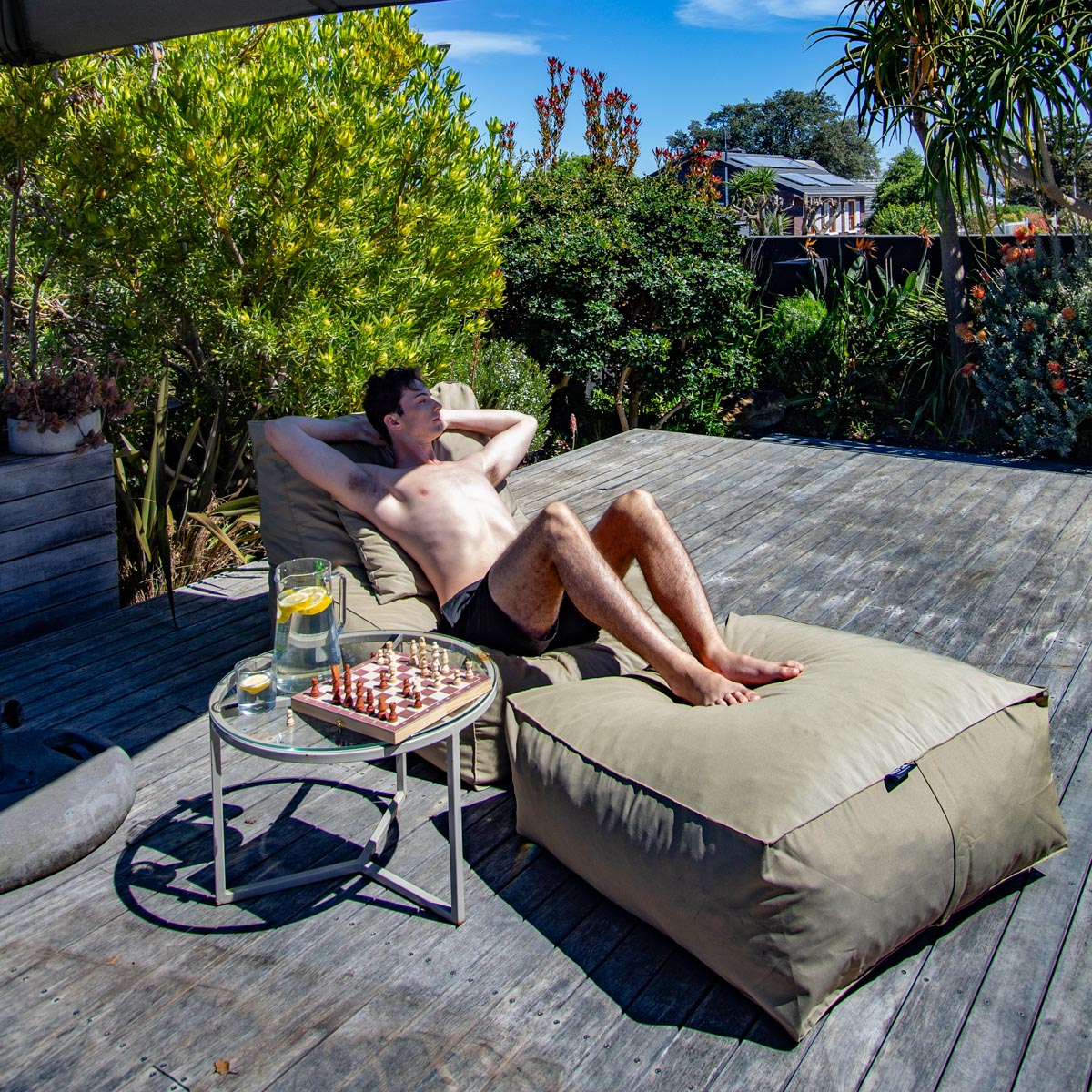 Man relaxing on a lounge chair with a chessboard and drink on a patio