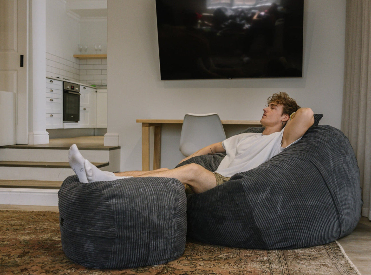 Man sitting on cell phone on large charcoal corduroy beanbag