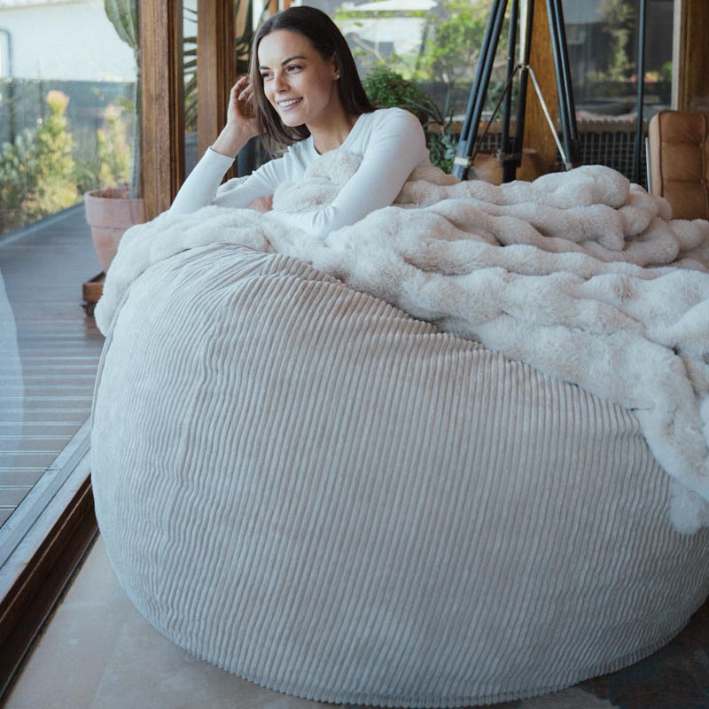 Woman sitting on a large bean bag chair with a blanket in a modern indoor setting.