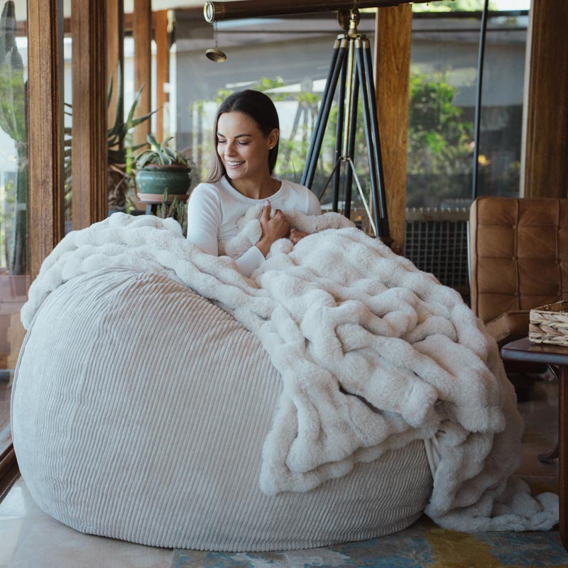 Woman sitting on a bean bag chair with a white blanket in a cozy living room.