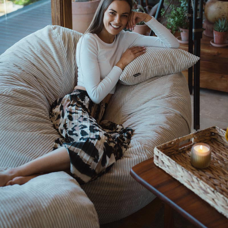 Woman sitting on a bean bag chair in a cozy living room with plants and a candle.