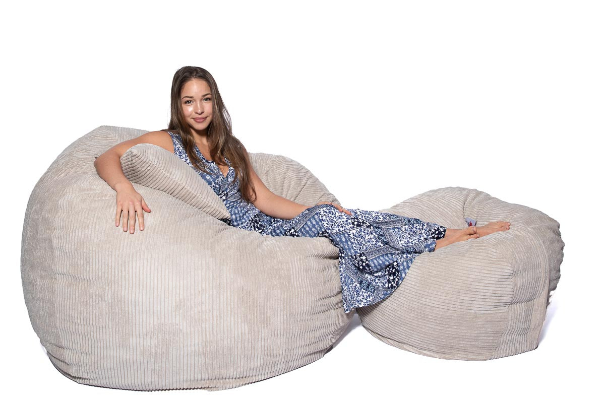 A person sitting comfortably on a large cream-colored corduroy bean bag chair.