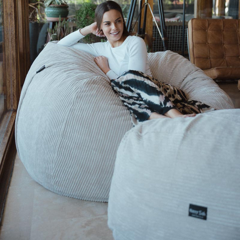 Woman sitting on a bean bag chair in a modern indoor setting with large windows.