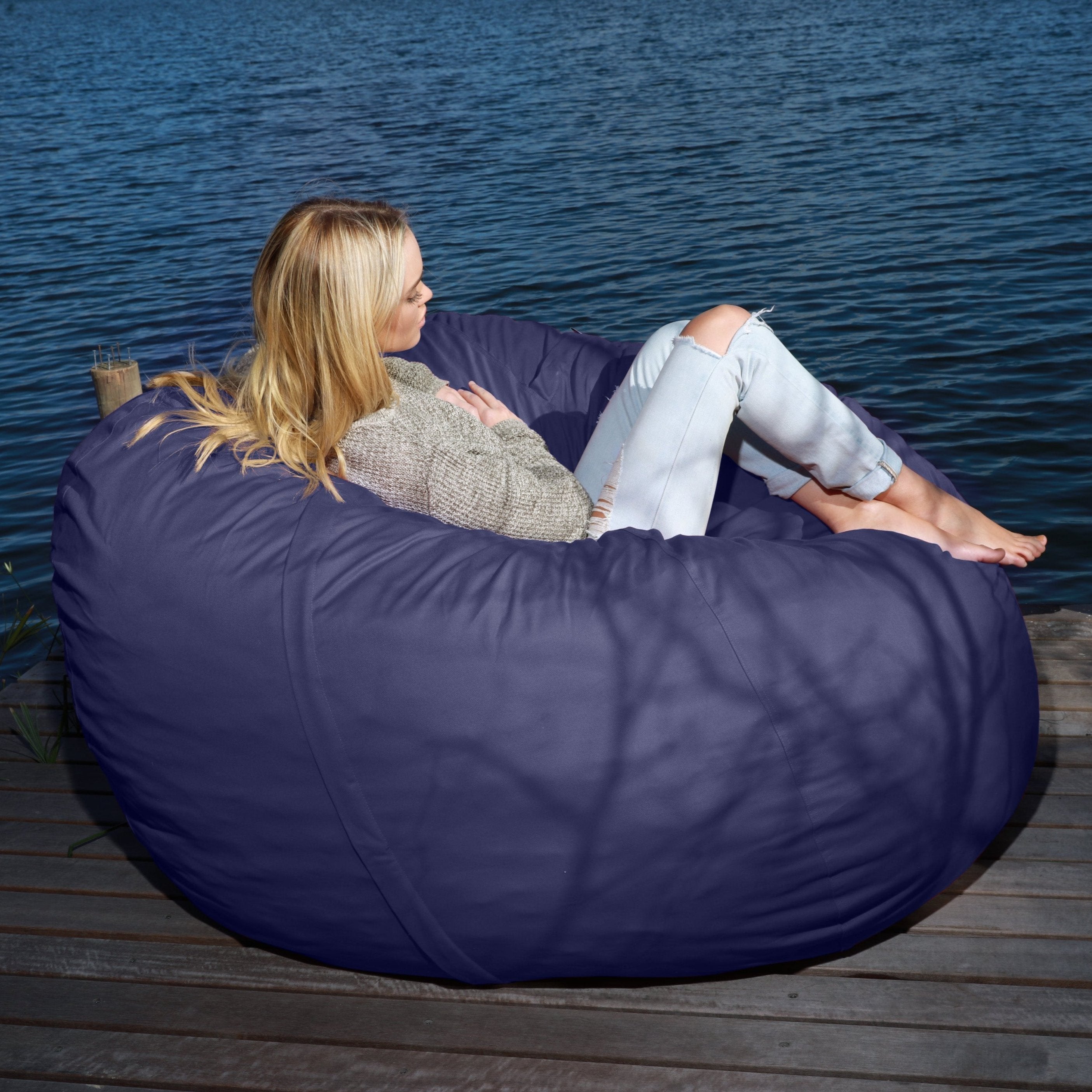 A person sitting on a navy blue bean bag chair outdoors by a body of water.