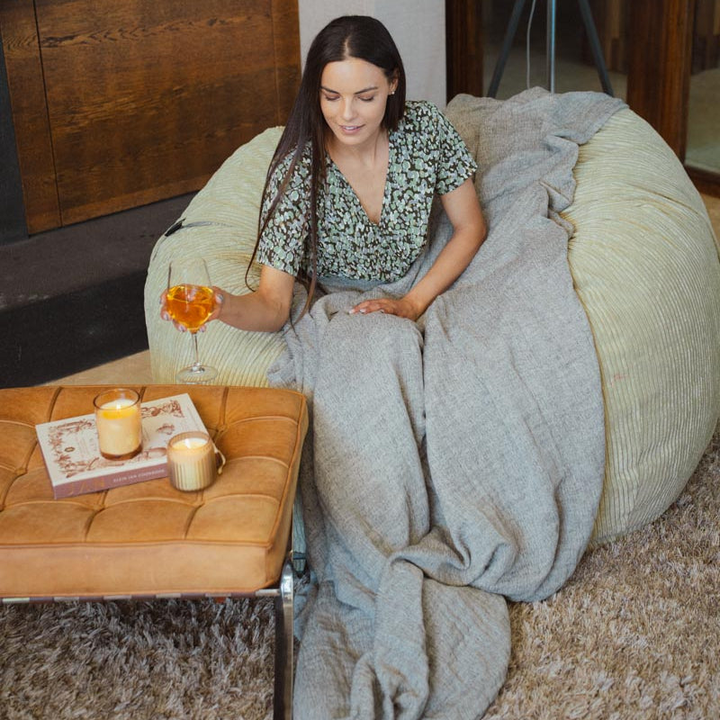 Woman sitting on a bean bag chair with a blanket, holding a glass of wine in a cozy room.