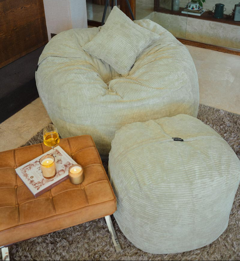 Large beige bean bag chair with ottoman in a living room setting.