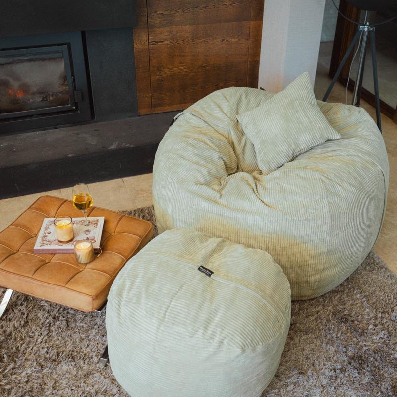 Two beige bean bags on a carpeted floor with a small table and items nearby.