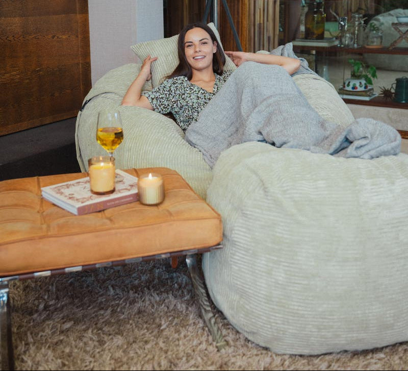 Woman relaxing on a bean bag chair in a cozy living room with candles and a glass of wine.