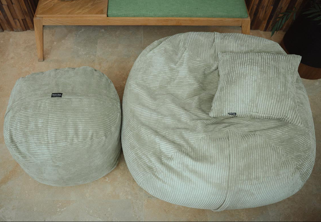 Two green bean bags on a beige floor with a wooden table in the background.