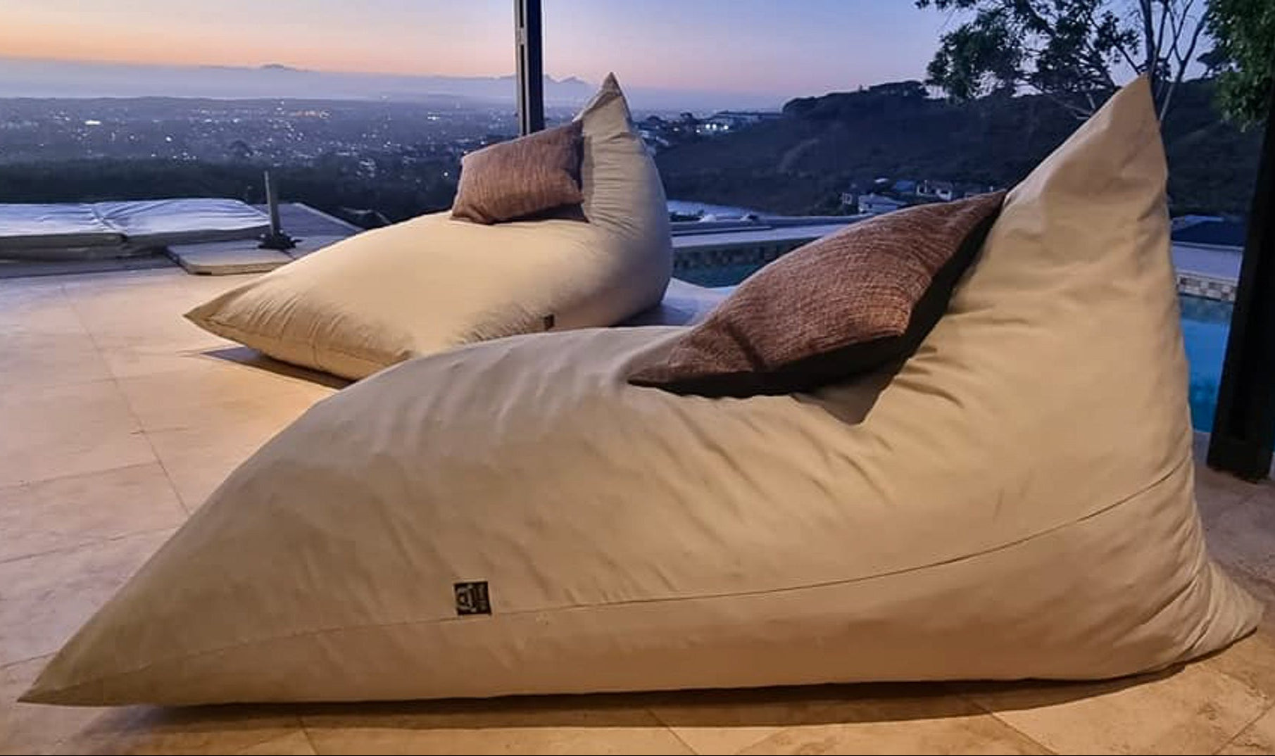 Beige bean bag chairs with brown cushions on a patio with a scenic view.