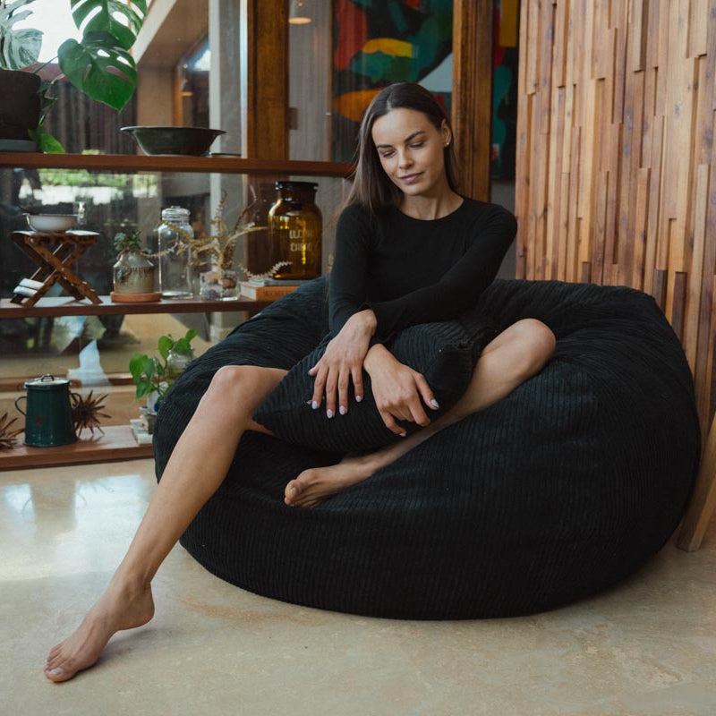 Woman sitting on a black bean bag chair in a modern indoor setting with wooden walls and decor.