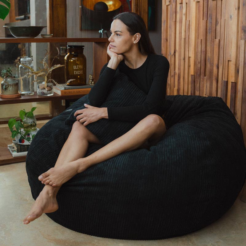 Woman sitting on a black bean bag chair in a room with wooden walls and a colorful abstract painting.
