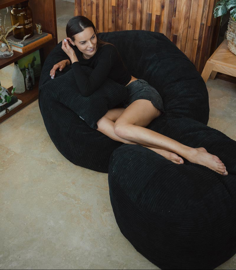 Woman sitting on a large black bean bag chair in a cozy room.