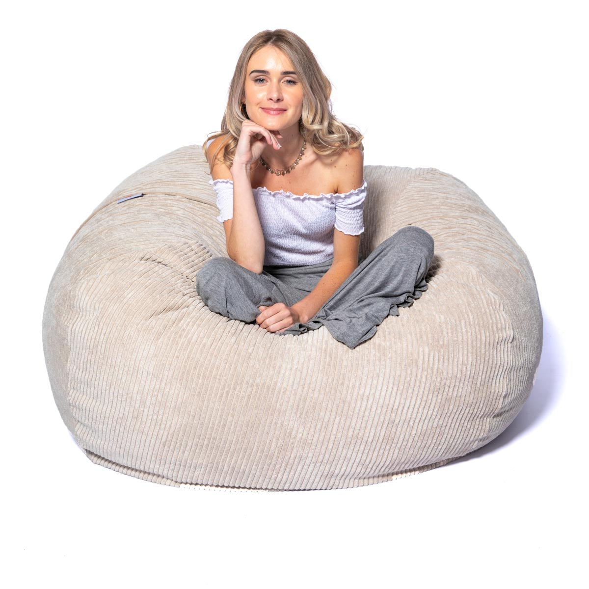 Woman sitting on a large beige bean bag chair against a white background
