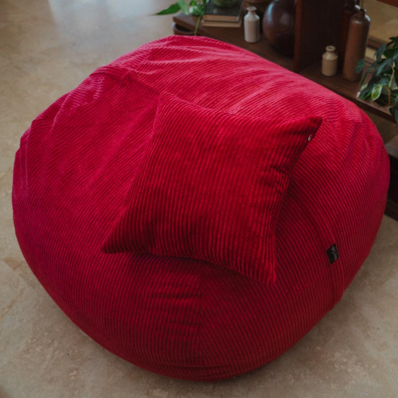 Red bean bag chair with a pillow on a beige floor