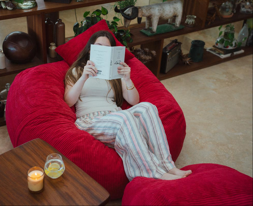 Person reading a book on a red bean bag chair in a cozy living room.