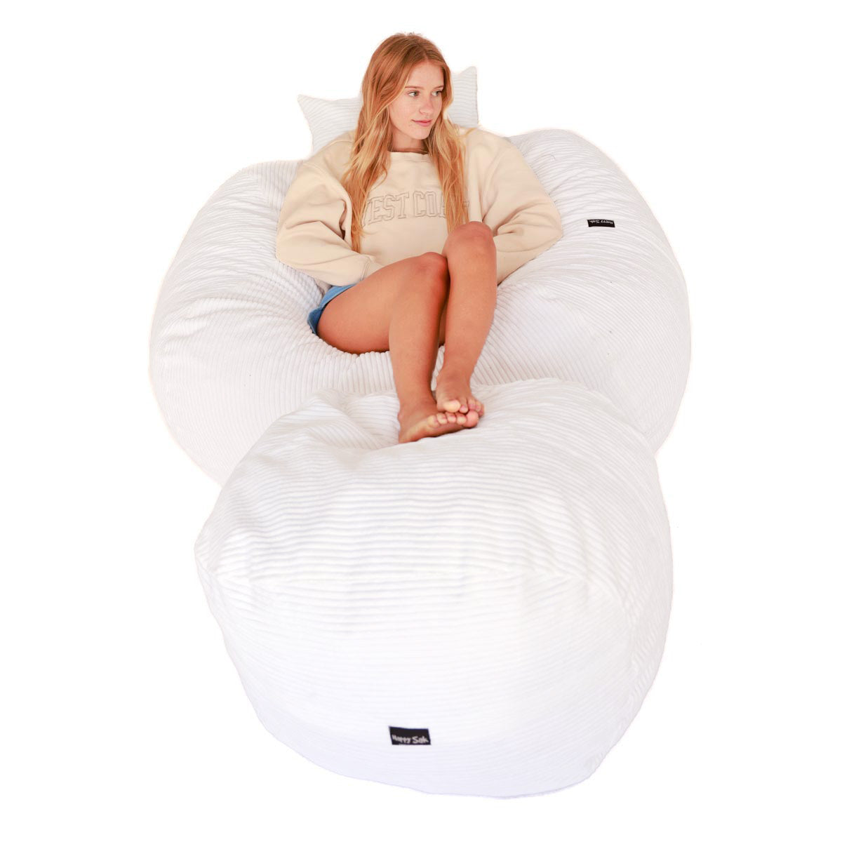 Person sitting on a large white bean bag chair with a visible brand logo.